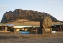 濟州島城山日出峰與入口的石碑，背景是海邊突起的火山口