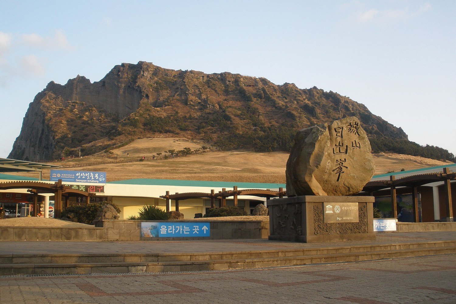 濟州島城山日出峰與入口的石碑，背景是海邊突起的火山口